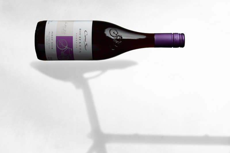 A bottle of wine with a purple lid, lays horizontally on the silhouette of a bicycle