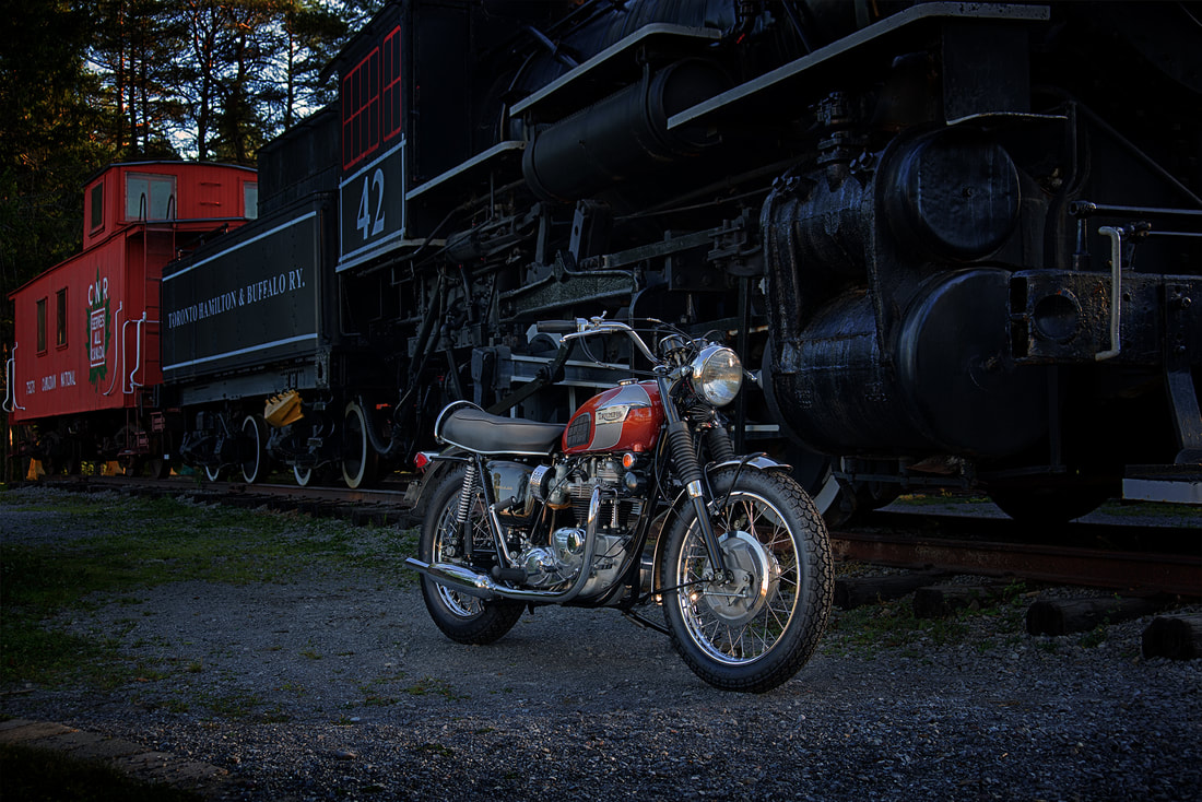 A photo of a motorcycle in front of a vintage coal powered train.
