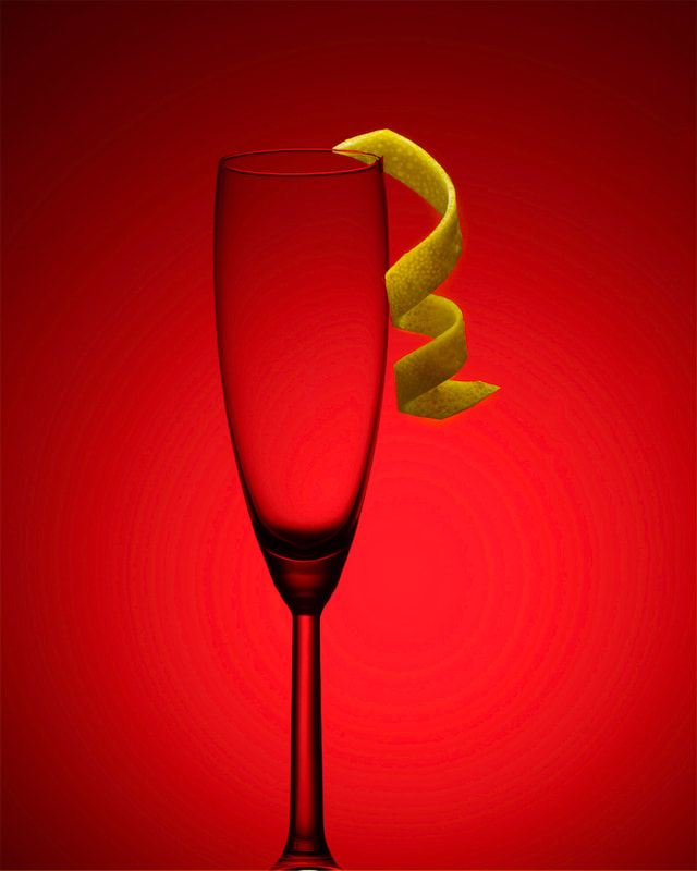 A tall champaign glass with a lemon twist garnish, sits in front of a red background.