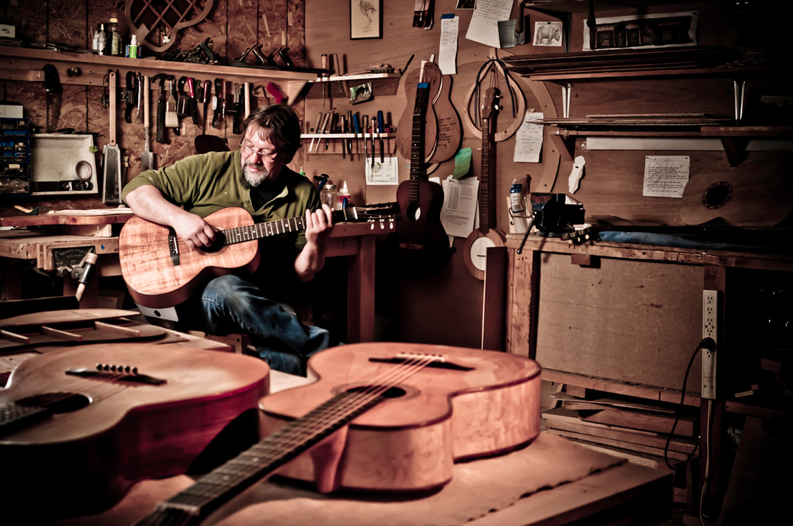 A man sits in a workshop playing a beautiful acoustic guitar.
