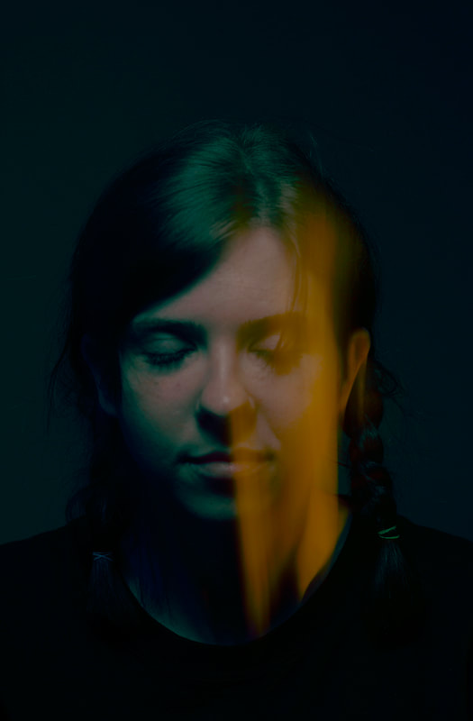 A closeup image of the face of a young woman. There is a streak of blurred light moving vertically down the image, partially obscuring her face.