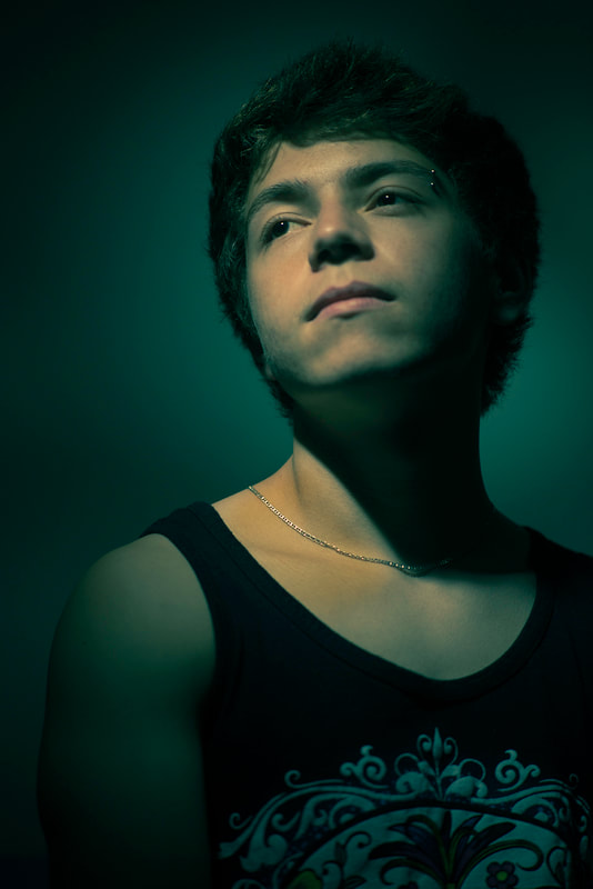 A teenage boy is illuminated with moody, almost creepy greenish light.