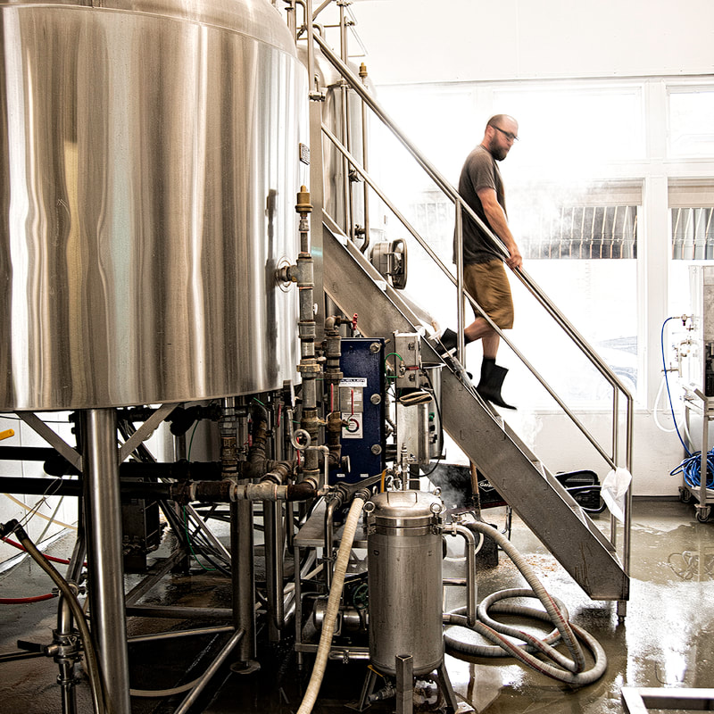A brewery worker is shown descending the metal stairs from a brewing tank.