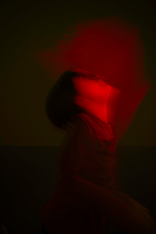 A young person has tilted their head backwards. They are brightly illuminated with a red light. The image is blurry.