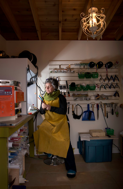 A portrait of a female artisan sitting at her work table, examining her crafting supplies.