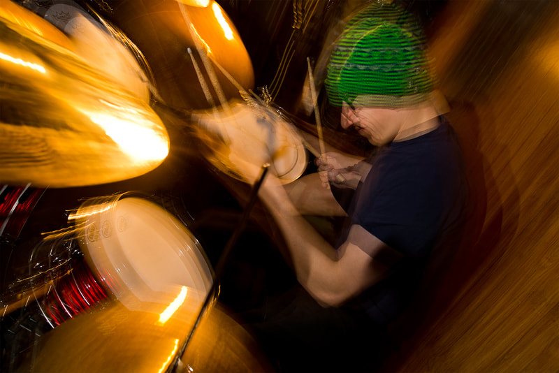 A drummer plays his drums quickly, his hands are quite blurry.