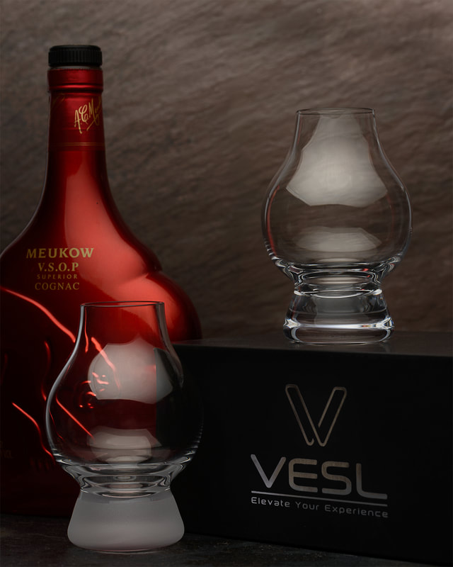 A photo of a pair of small drinking glasses along with a red Cognac bottle. They are lit from the tip in a dramatic fashion. The image is shot by photographer Mike Taylor in his Peterborough Ontario studio.