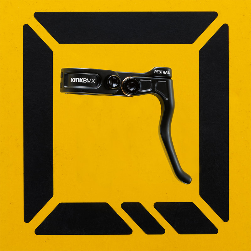 A slick black bicycle brake lever is framed by a bold black logo on a yellow surface. Shot by amazing product photographer, Mike Taylor of Peterborough Ontario, Canada.