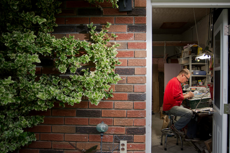 A man in a red sweater works within a room. The exterior is a red brick wall partly covered with a green vine.