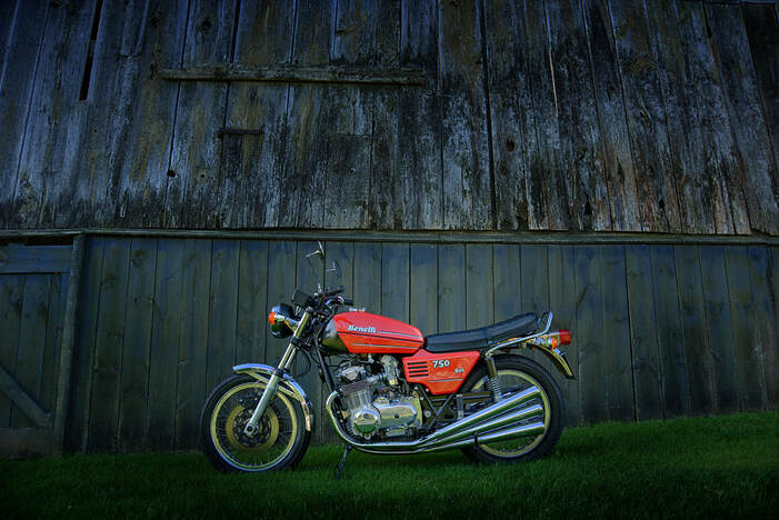 A red motorcycle stands in front of a dilapidated old barn