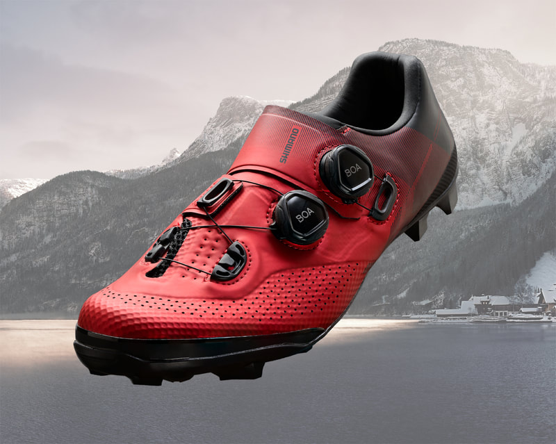 An image of a red cycling shoe in front of a monochromatic mountain scene.