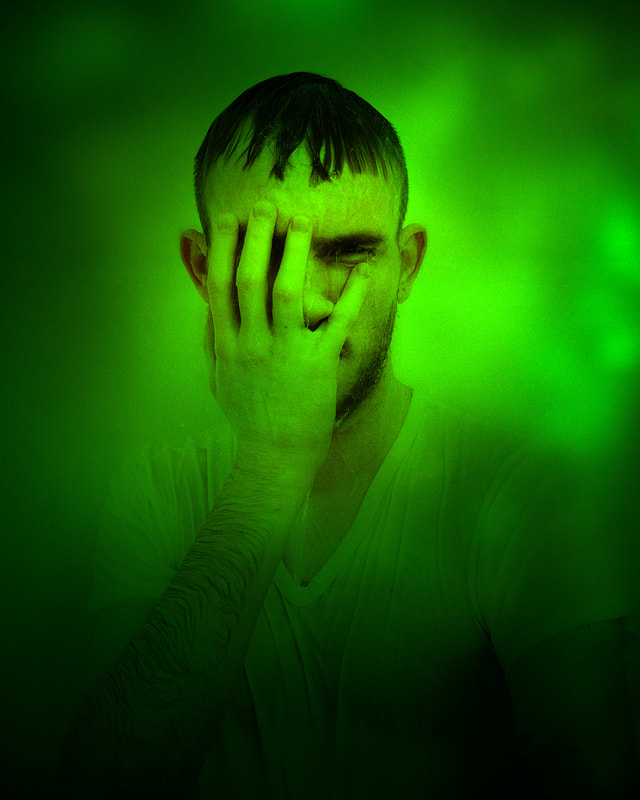 A green toned portrait of a man with his hand on his face.